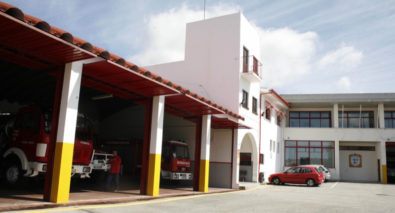 O quartel da 4.ª Companhia do Louriçal: sob um alpendre de telha vermelha assente em pilares brancos com a base amarela, três viaturas dos Bombeiros Voluntários de Pombal nas garagens abertas. Um bombeiro de farda vermelha atravessa o alpendre. À direita, o edifício de dois pisos, branco com caixilharia vermelha, com o emblema da corporação na parede.
