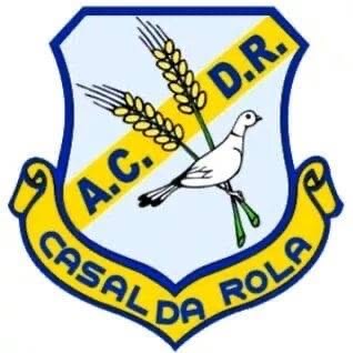 Emblema da Associação Cultural, Desportiva e Recreativa do Casal da Rola: um escudo azul-claro atravessado por uma faixa azul-escura com as iniciais A.C.D.R., duas espigas douradas e uma pomba branca de asas fechadas. Em baixo, uma fita amarela com o nome Casal da Rola.