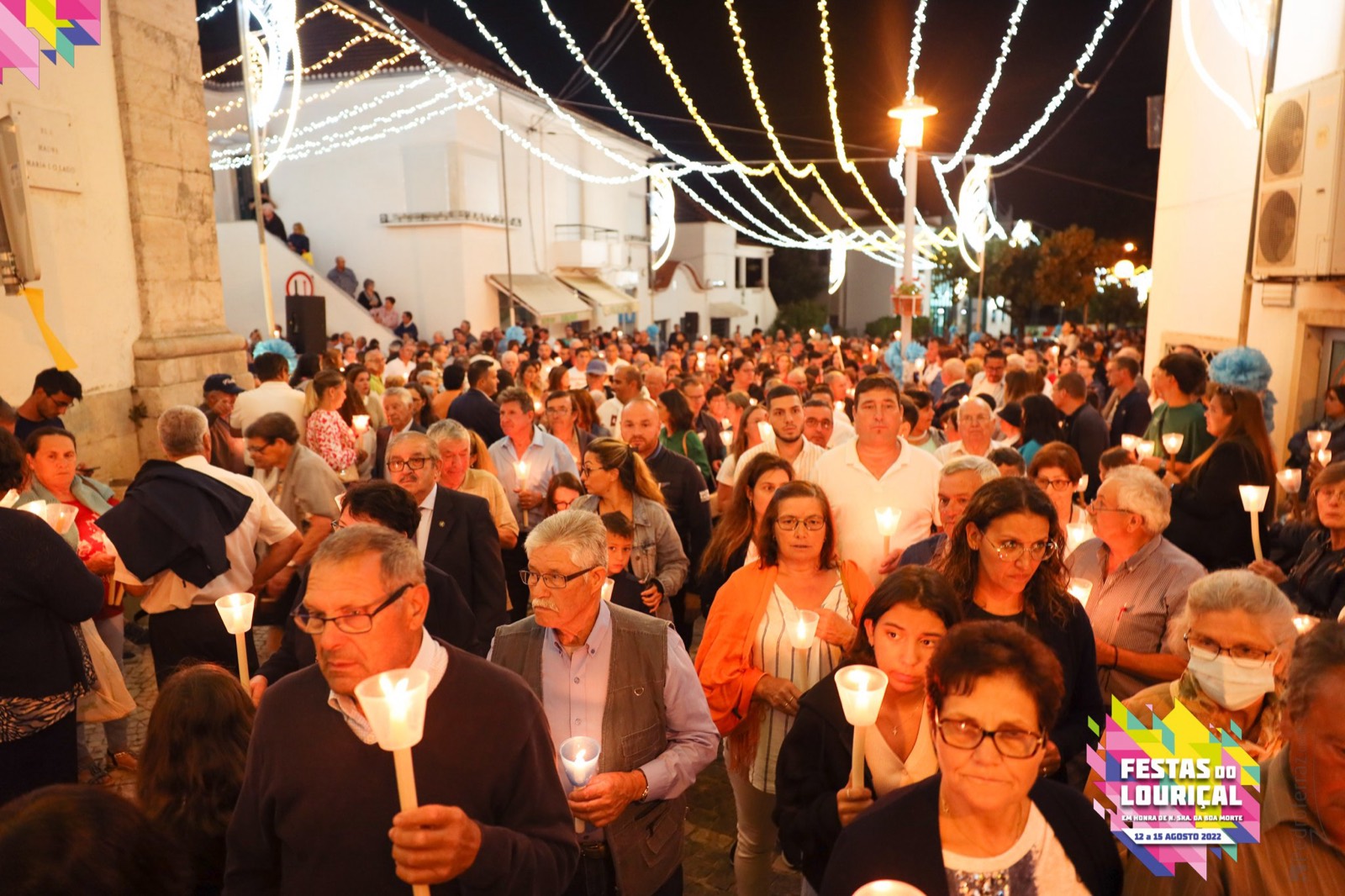 A Procissão das Velas a passar pelas ruas do Louriçal ao anoitecer: a rua cheia de gente, cada pessoa com uma vela acesa na mão, sob os fios de luzes que atravessam a rua de um lado ao outro.